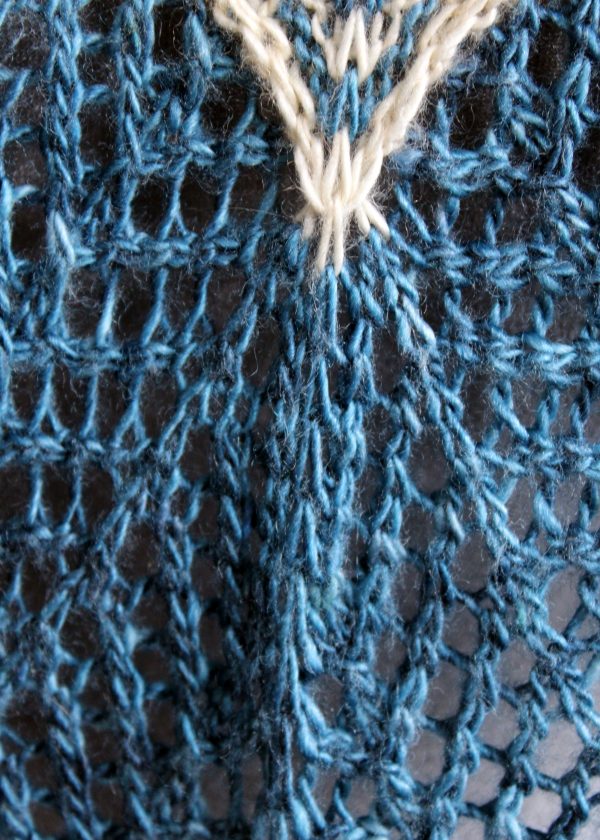 A close up on the spine of a cowlette with a mosaic body, knit in blue and white yarn, with a wide lace border knit in blue.