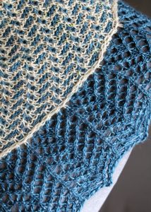 A close up on a cowlette with a mosaic body, knit in blue and white yarn, with a wide lace border knit in blue.