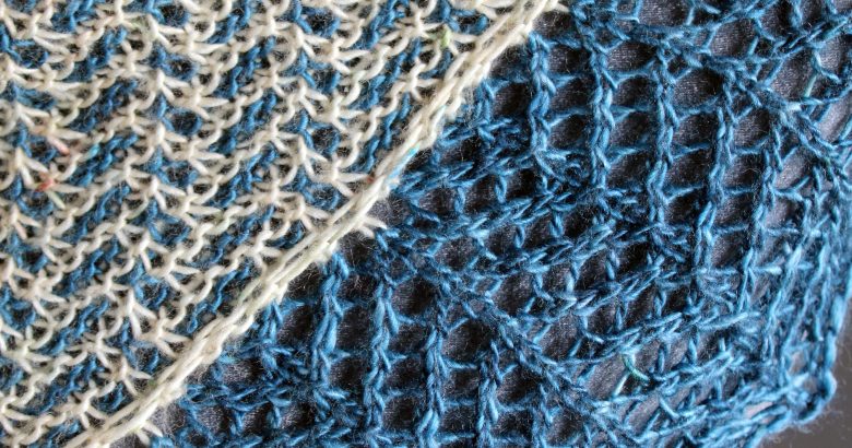 A close up on a cowlette with a mosaic body, knit in blue and white yarn, with a wide lace border knit in blue.
