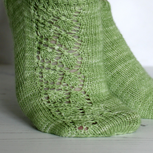 A pair of modelled short socks featuring a lace leaf column running up the outside of the foot, knit in green yarn.