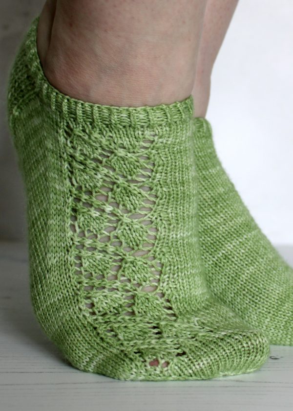 A pair of modelled short socks featuring a lace leaf column running up the outside of the foot, knit in green yarn.