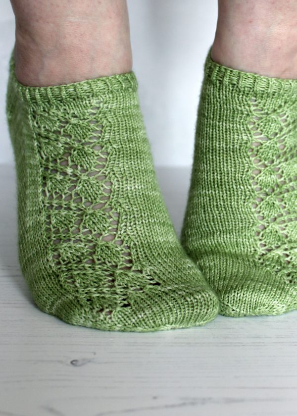 A pair of modelled short socks featuring a lace leaf column running up the outside of the foot, knit in green yarn.