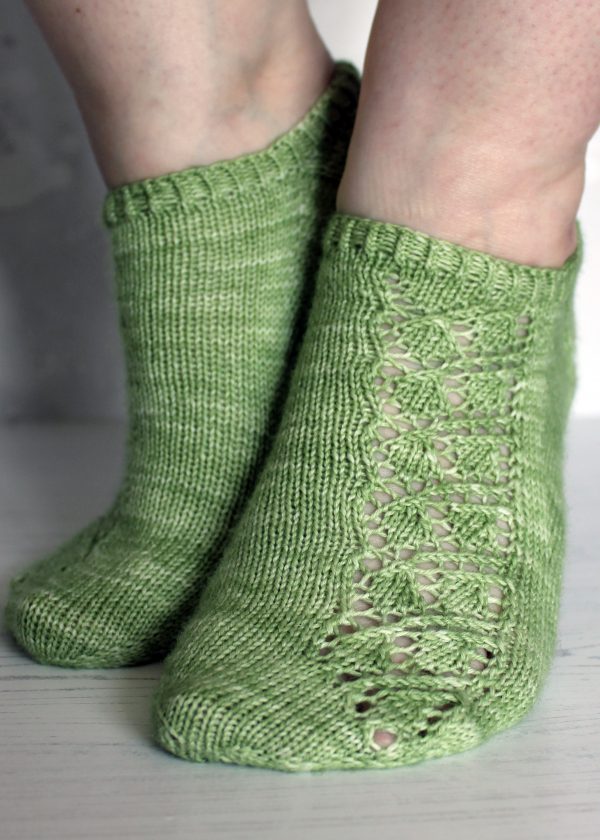 A pair of modelled short socks featuring a lace leaf column running up the outside of the foot, knit in green yarn.