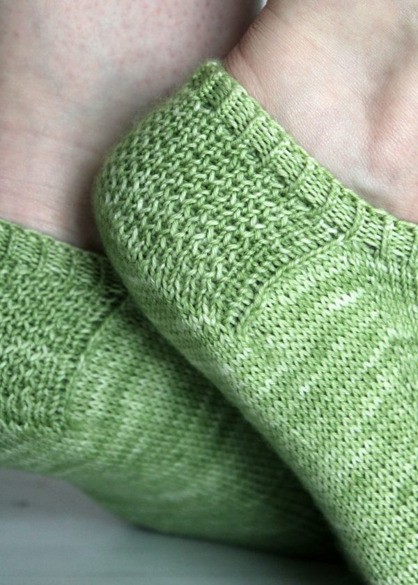A pair of modelled short socks showing the textured eye of partridge heels, knit in green yarn.