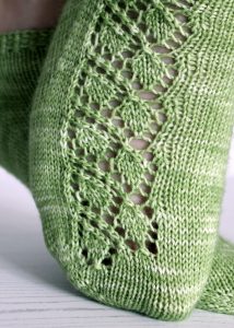 A close up on the toe of short socks featuring a lace leaf column running up the outside of the foot, knit in green yarn.