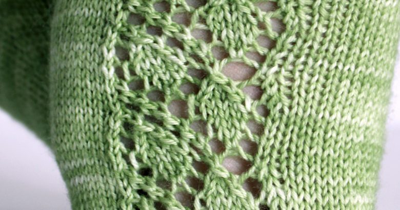 A close up on the toe of short socks featuring a lace leaf column running up the outside of the foot, knit in green yarn.