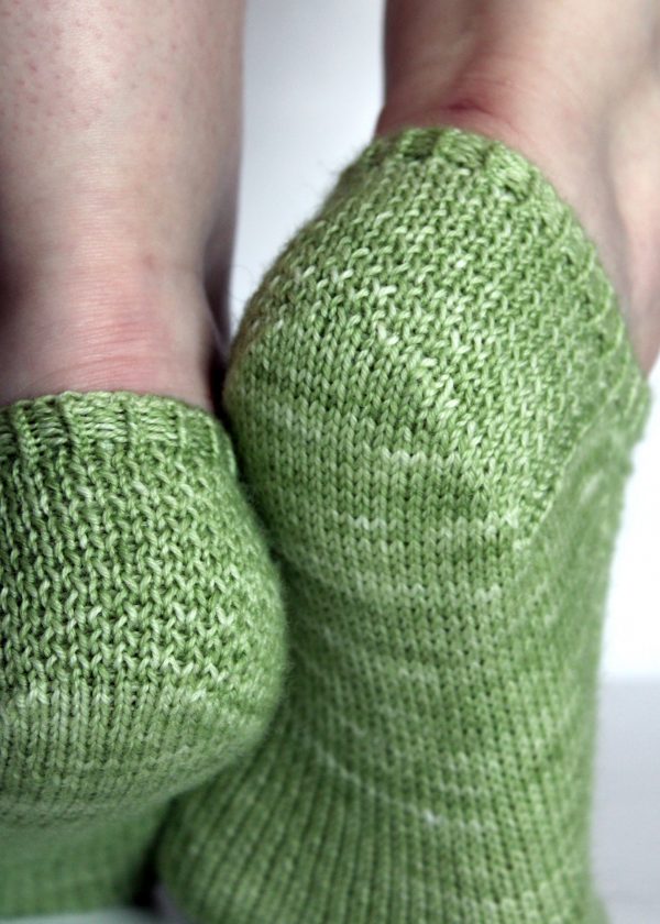 A pair of modelled short socks showing the textured eye of partridge heels, knit in green yarn.