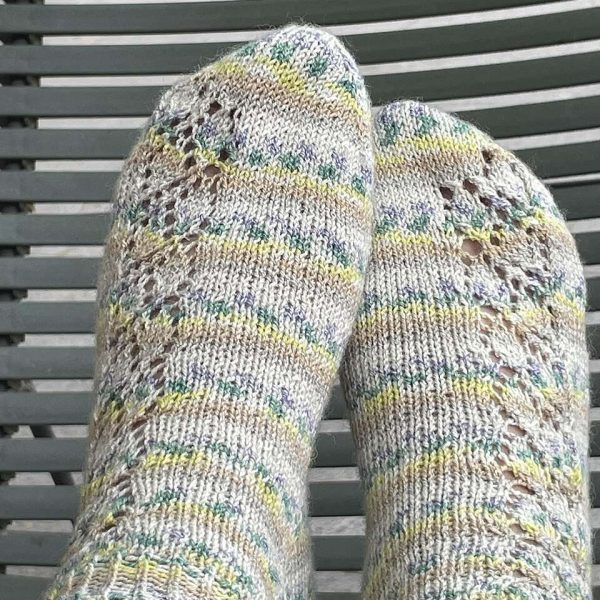 A pair of short socks featuring a lace leaf column running up the outside of the foot, knit in a self striping yarn.