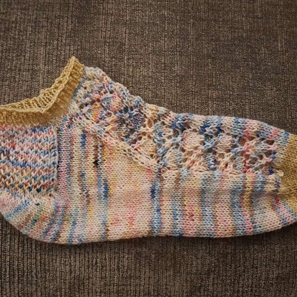 A short sock featuring a lace leaf column running up the outside of the foot, knit in a variegated yarn.