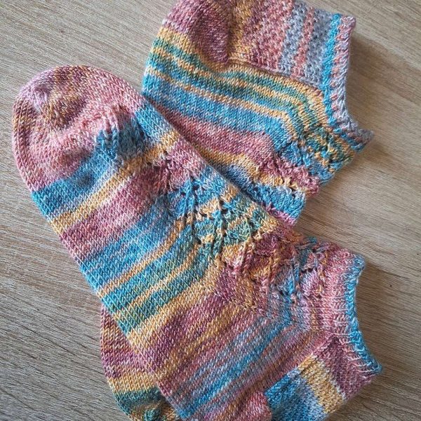 A pair of short socks featuring a lace leaf column running up the outside of the foot, knit in a striped yarn.