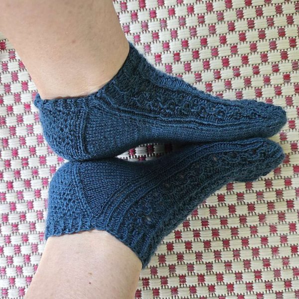 Two modelled short (trainer) socks with a twisted rib and lace pattern covering the top of the foot. The socks are knit in navy yarn.