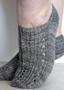 Two modelled short (trainer) socks with a twisted rib and lace pattern covering the top of the foot. The socks are knit in grey yarn.